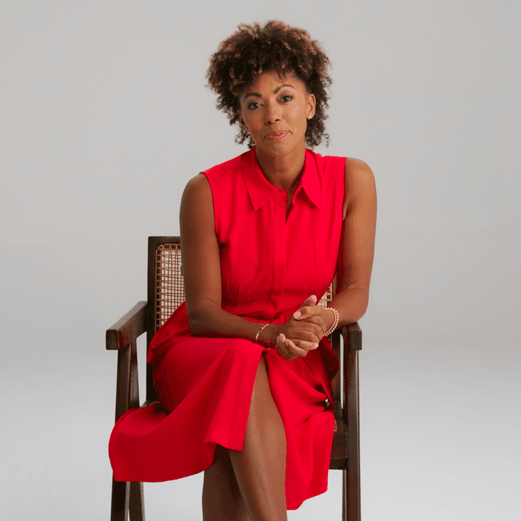 Dr Zoe Williams seated, wearing a bright red dress, and looking at the camera elegantly.