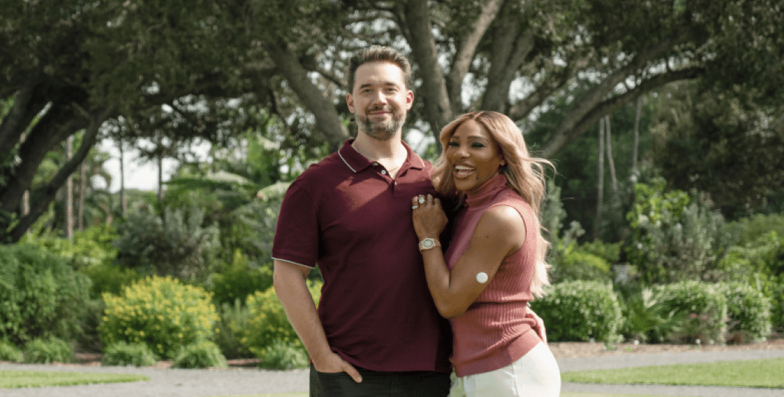 A photograph of Serena Williams and Alexis Ohanian standing together in a grassy field. 