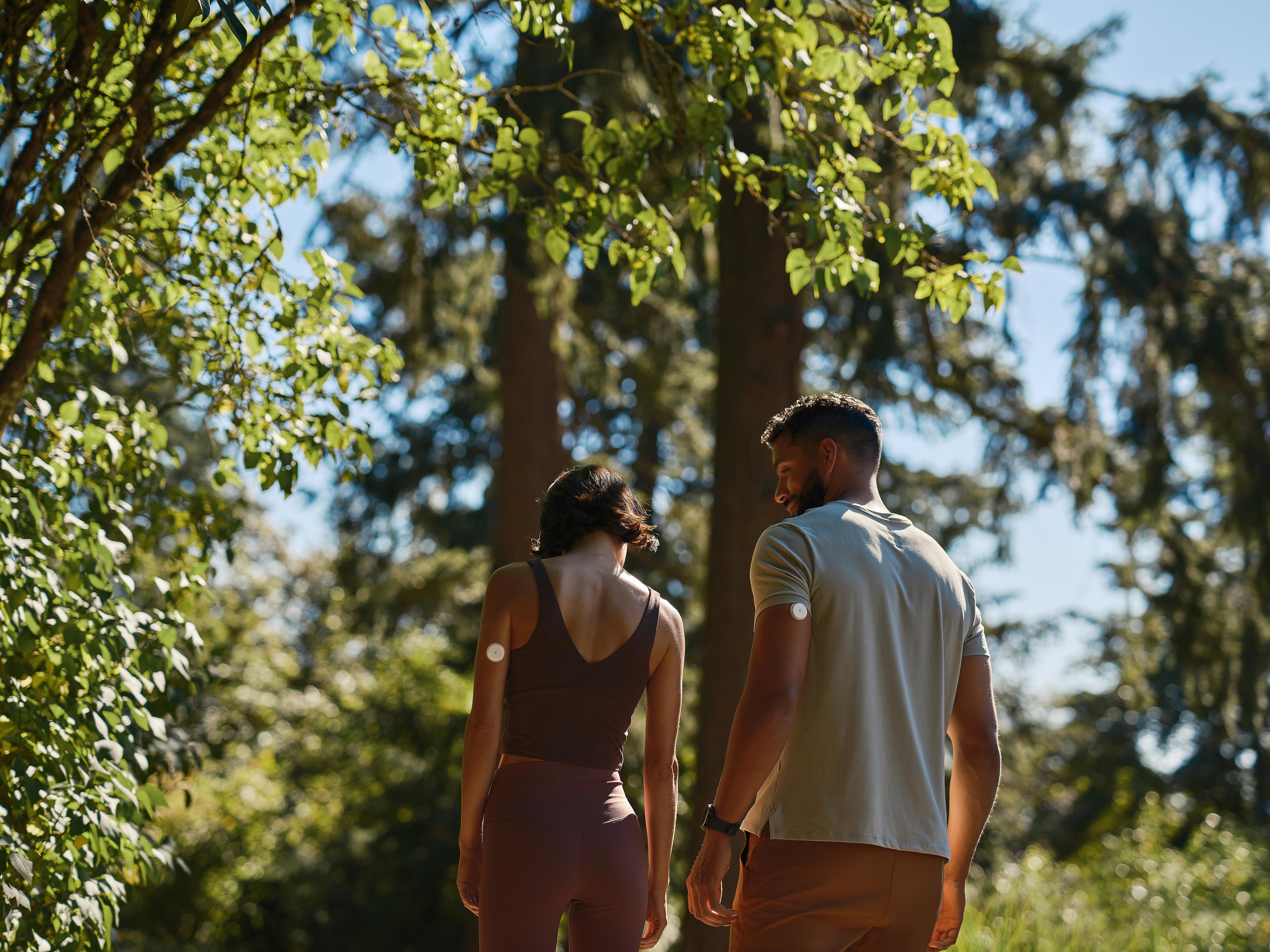 Two people walking in calm park setting wearing glucose monitors