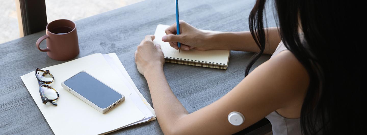 Woman writing on paper wearing glucose monitor