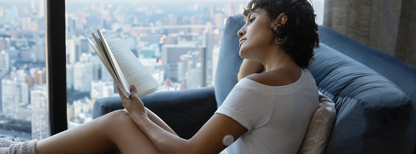 Woman in a high-rise apartment reading a book wearing a CGM