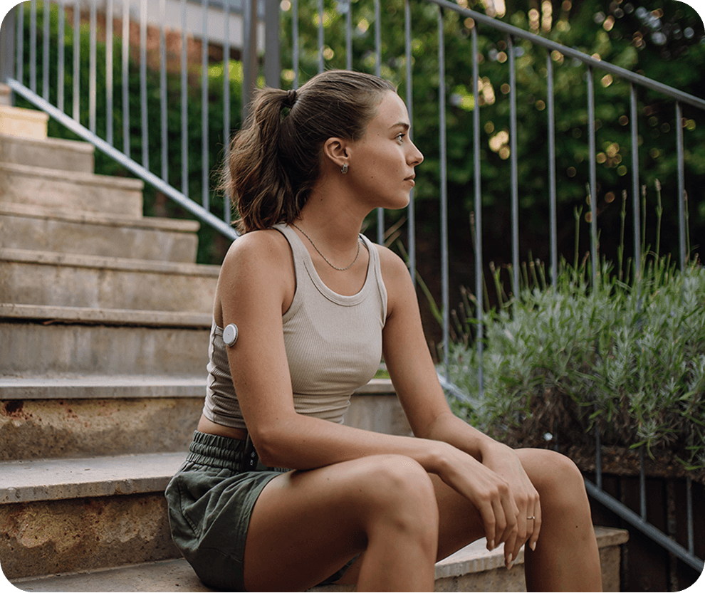 A person wearing a Lingo CGM sitting on some stairs outside