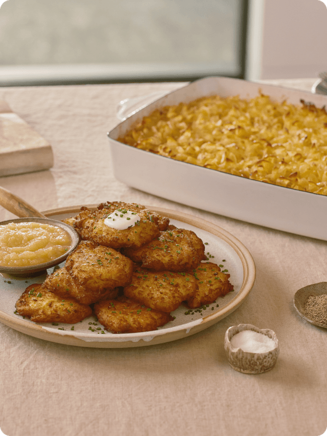 Latkes balanced on plate with a casserole of macaroni and cheese 