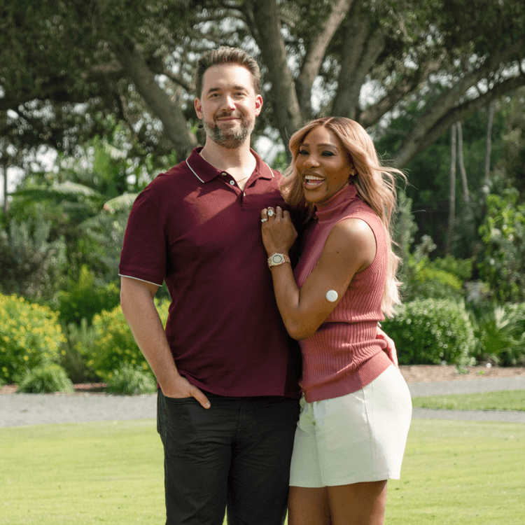 A photograph of Serena Williams and Alexis Ohanian standing together in a grassy field. 