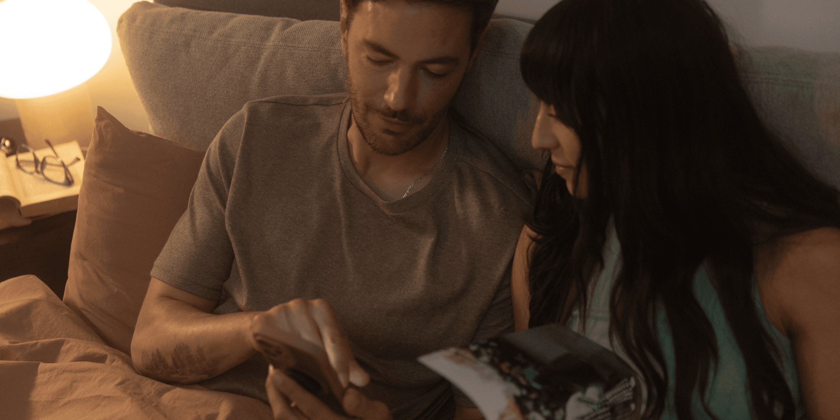 Couple in bed looking at smartphone.