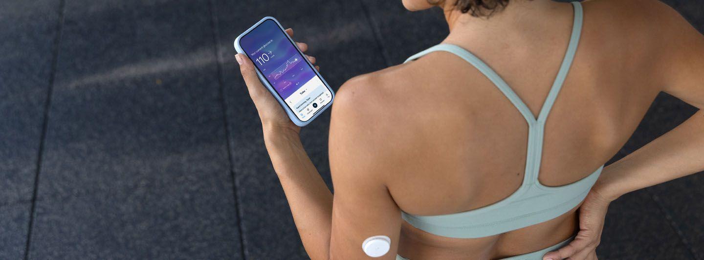 Woman in sportswear wearing a CGM and looking at the Lingo app